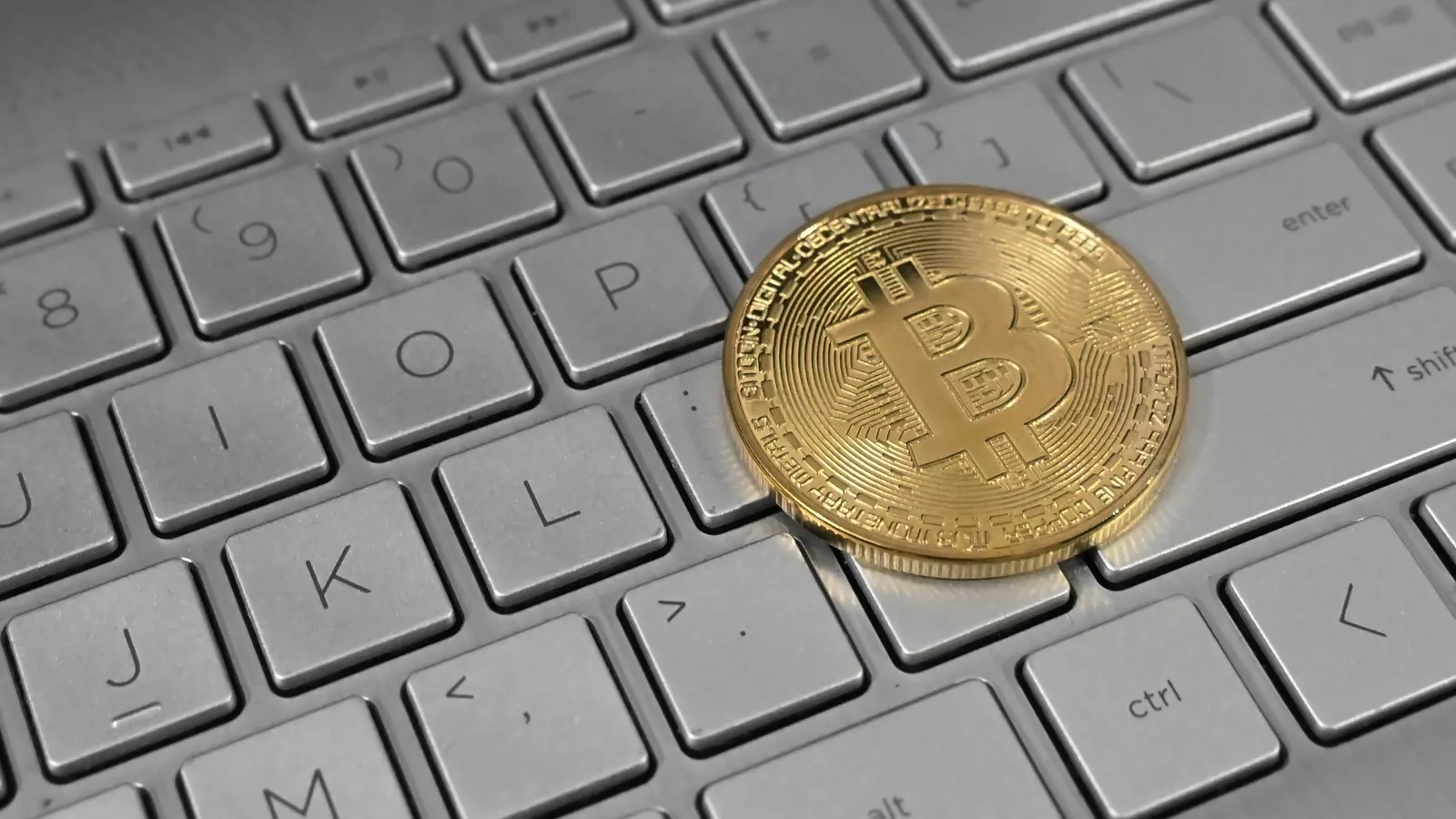 Bitcoin coin resting on a laptop keyboard, illustrating paying for a Minecraft alt with crypto